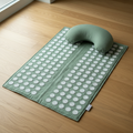 Sage green acupressure mat and neck pillow on oak hardwood floor
